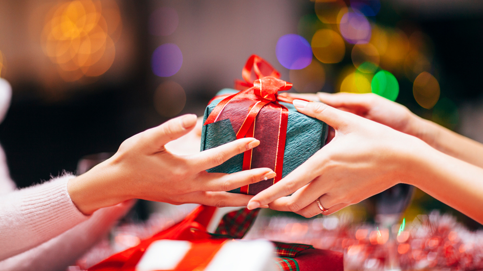 A wrapped present with a red bow is passed from one set of hands to another.