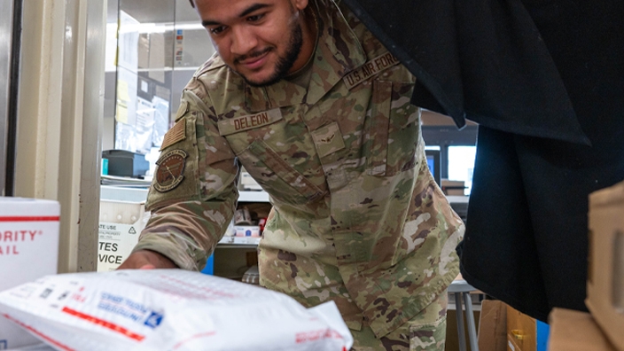 A young man in military garb handles USPS-branded packages