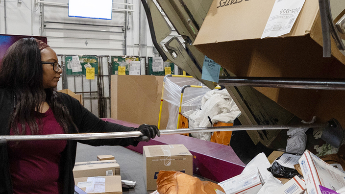 A woman processes packages on the workroom floor of a postal facility