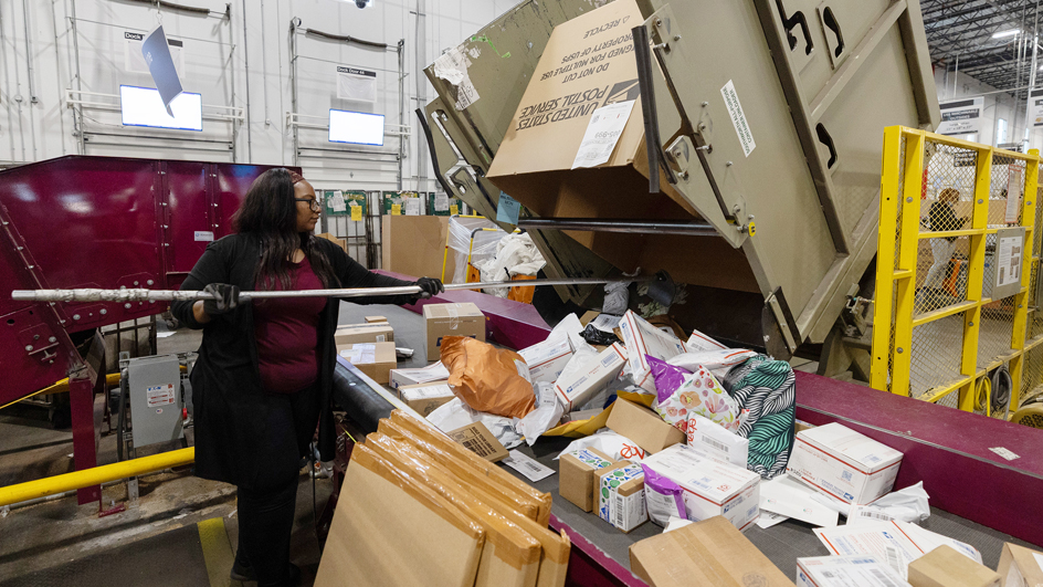 A woman processes packages on the workroom floor of a postal facility