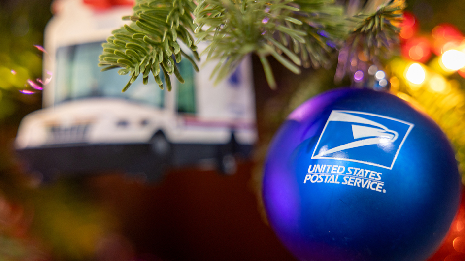 A blue ball bearing the Postal Service logo hanging on a Christmas tree branch