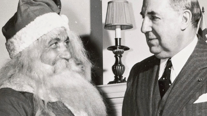 A black-and-white vintage photo of a man wearing a Santa Claus suit standing next to a man in a business suit