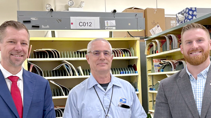 Three men stand next to each other in a Post Office workroom