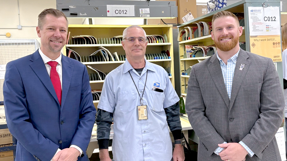 Three men stand next to each other in a Post Office workroom