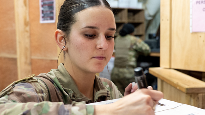 A woman in a military uniform examines a package with USPS branding