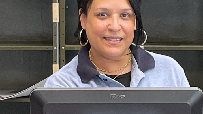 A woman in a Postal Service uniform stands at a Post Office retail counter