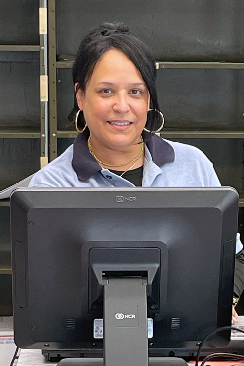 A woman in a Postal Service uniform stands at a Post Office retail counter