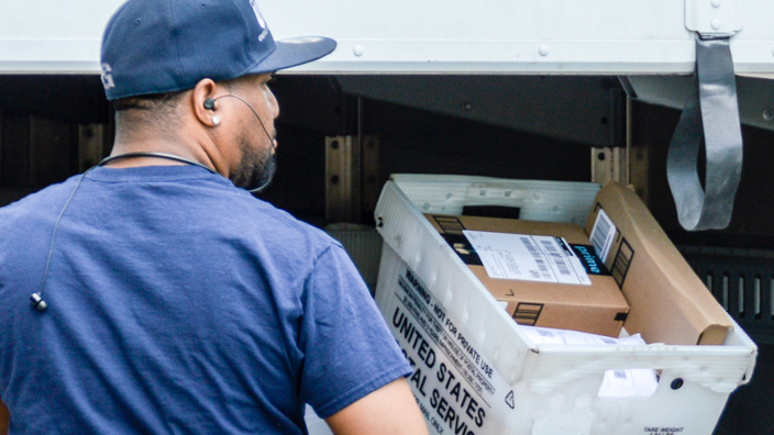 A postal worker loads a delivery vehicle from behind