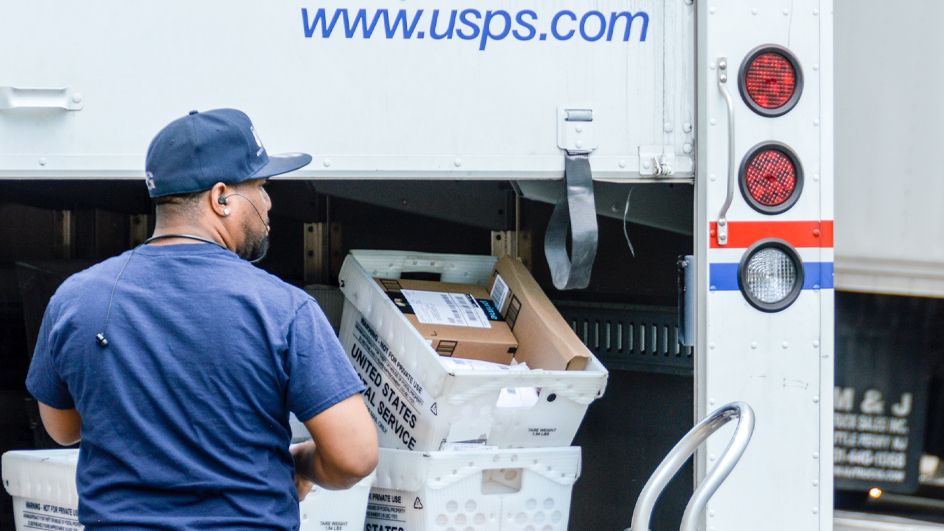 A postal worker loads a delivery vehicle from behind