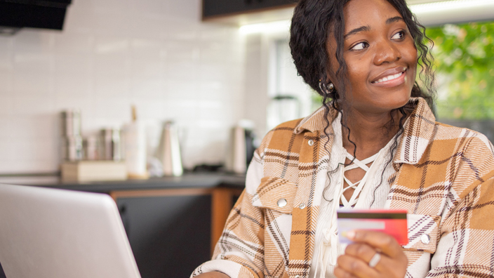 A woman sits at a kitchen table holding a debit card