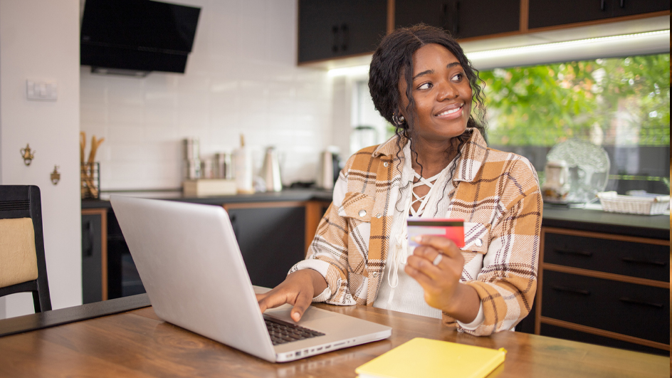 A woman sits at a kitchen table holding a debit card