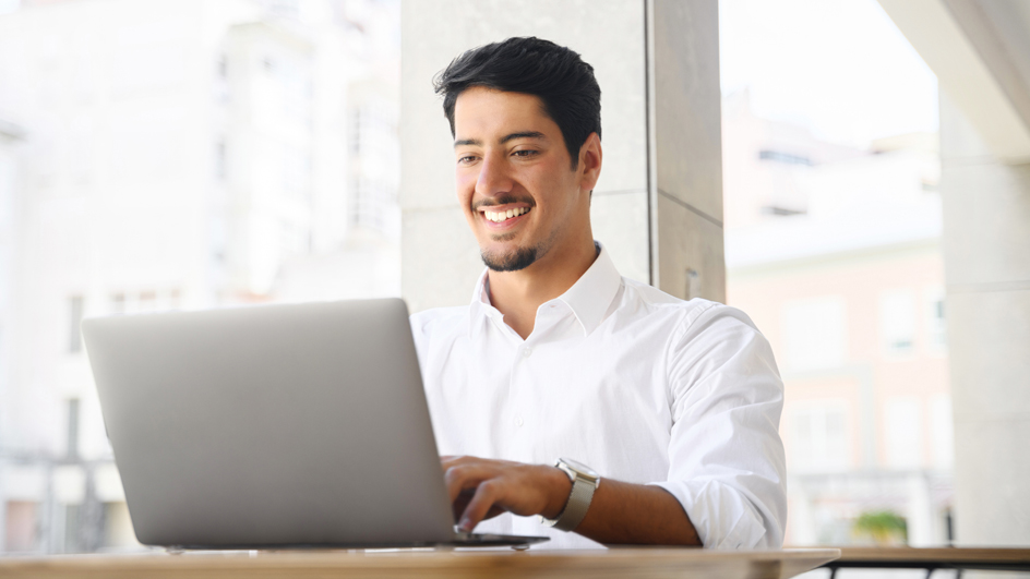 A man smiles as he sits in front of a computer monitor
