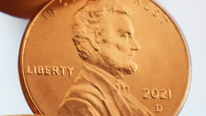 A close-up of a forefinger and thumb holding a shiny penny