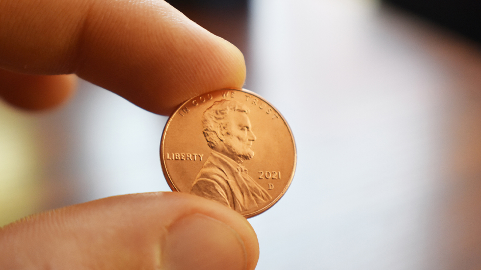A close-up of a forefinger and thumb holding a shiny penny