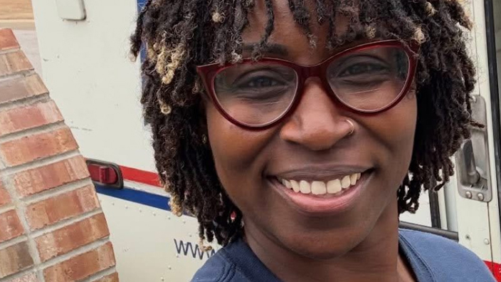 A woman wearing glasses and smiling standing in front of a delivery vehicle