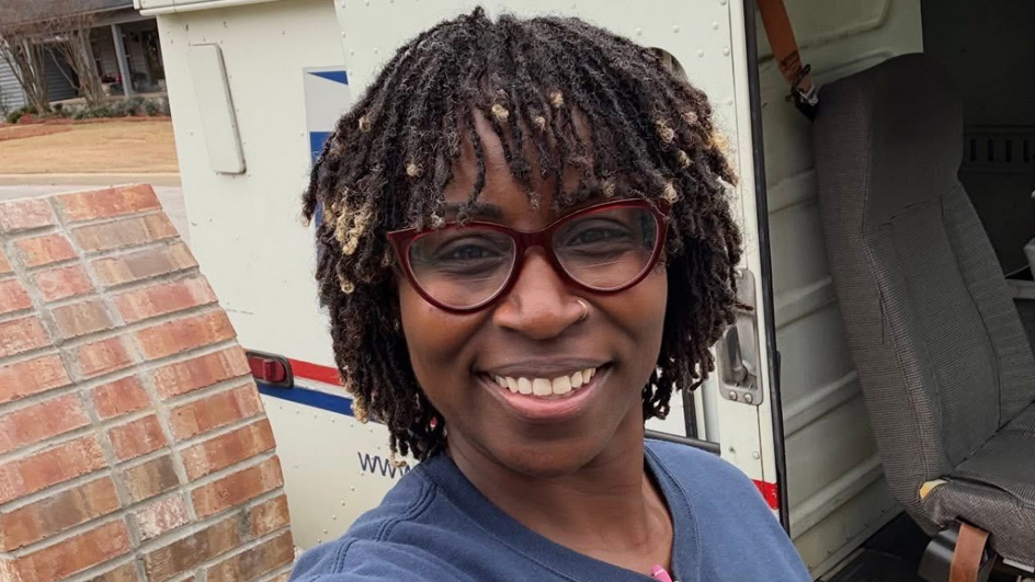 A woman wearing glasses and smiling standing in front of a delivery vehicle