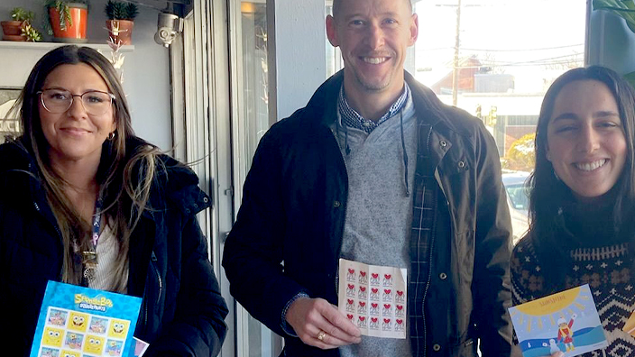 Three people standing in a row holding up postage stamps and cards for letter writing.