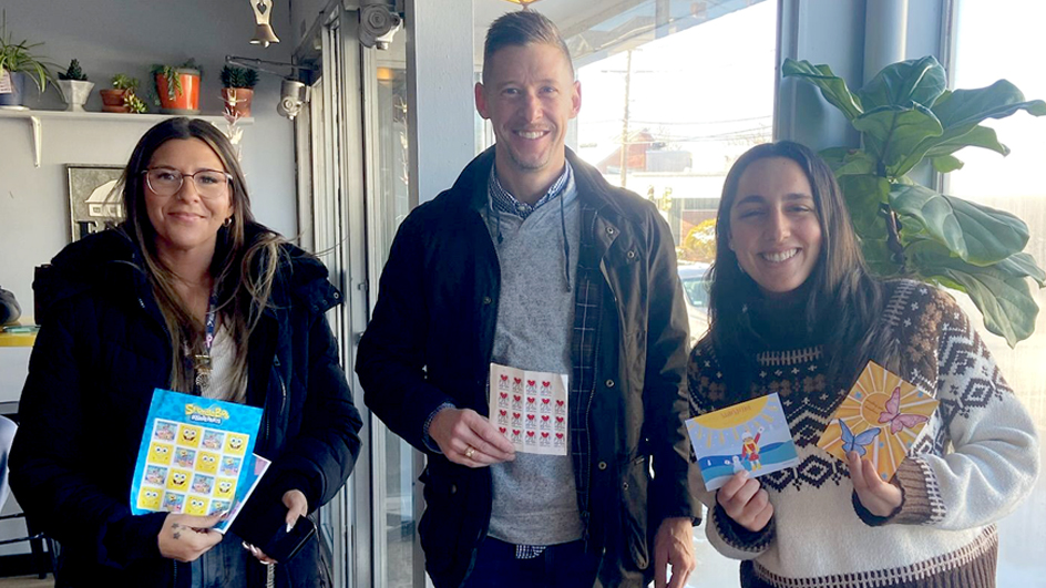 Three people standing in a row holding up postage stamps and cards for letter writing.