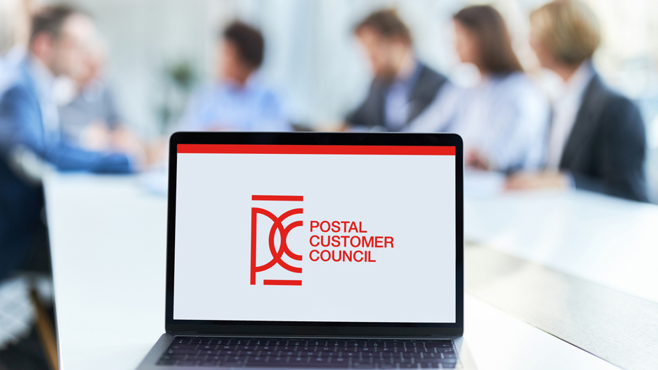 Postal customer council logo on a laptop screen with a blurred background of five people sitting around a table.