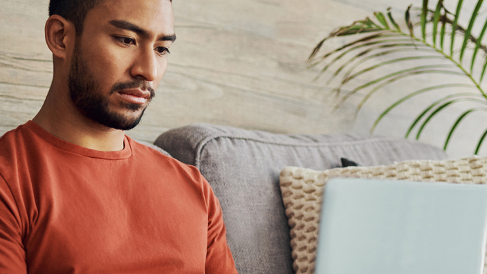 A man sits on his sofa and looks at his laptop