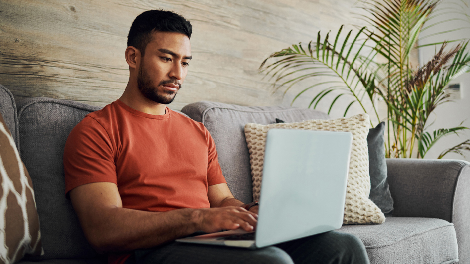 A man sits on his sofa and looks at his laptop
