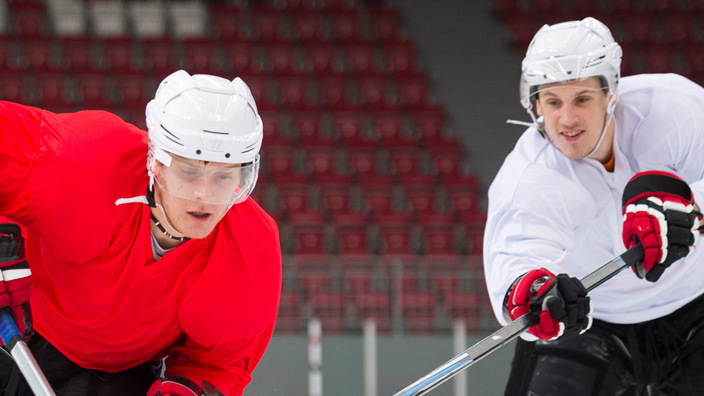 Three hockey players chasing a puck on an ice rink.