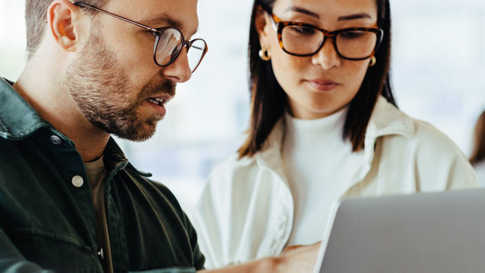 A man in a dark shirt and a woman in a white shirt look at a laptop screen.