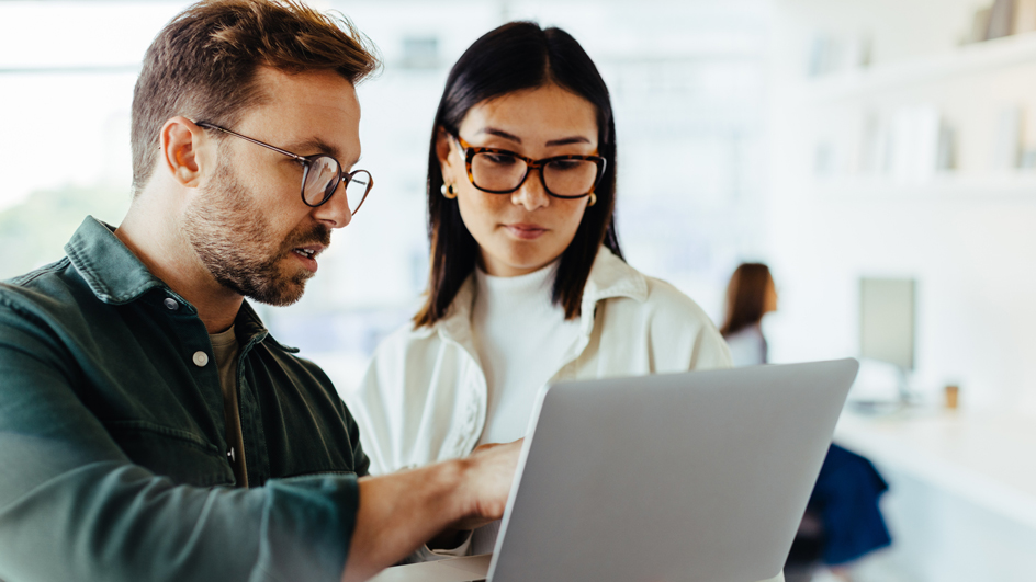 A man in a dark shirt and a woman in a white shirt look at a laptop screen.