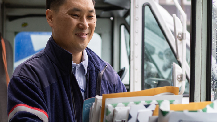 A letter carrier loads trays of mail into a postal delivery vehicle