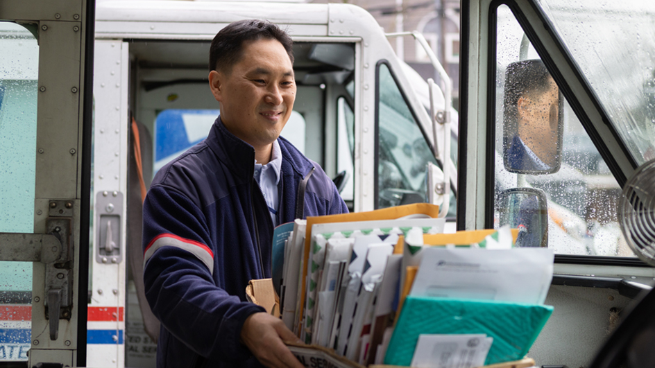 A letter carrier loads trays of mail into a postal delivery vehicle