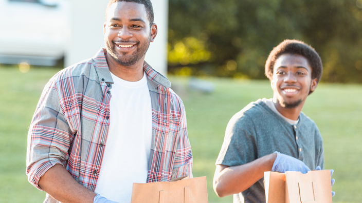An older man and a younger man hold bags of food donations