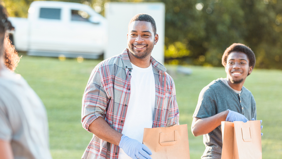 An older man and a younger man hold bags of food donations