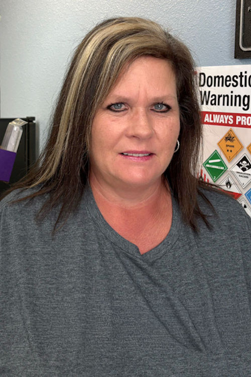 A woman wearing a USPS shirt stands in a Post Office workroom