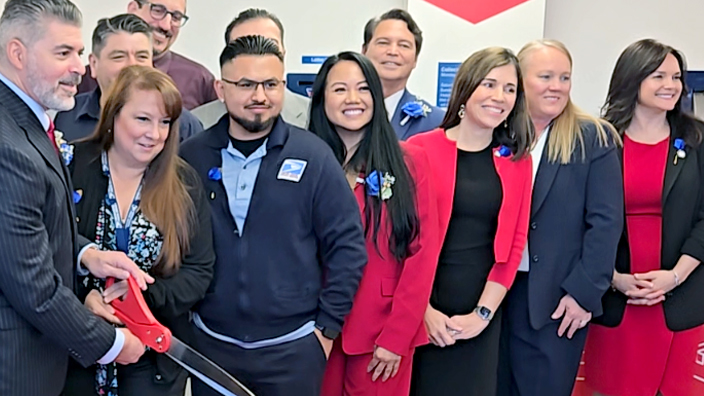 A large group of people standing behind a red ribbon as it is cut during a ceremony
