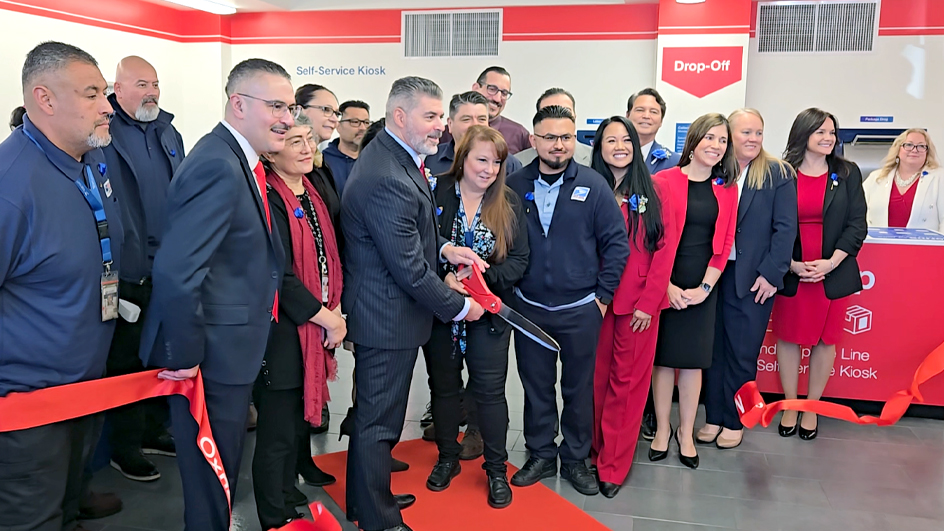 A large group of people standing behind a red ribbon as it is cut during a ceremony
