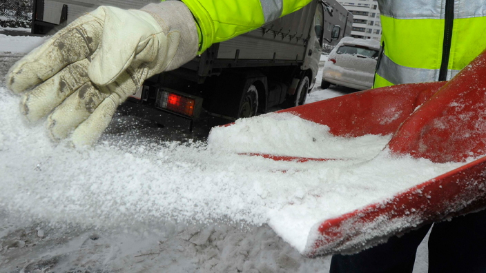 A worker spreads ice melt in a snowy environment