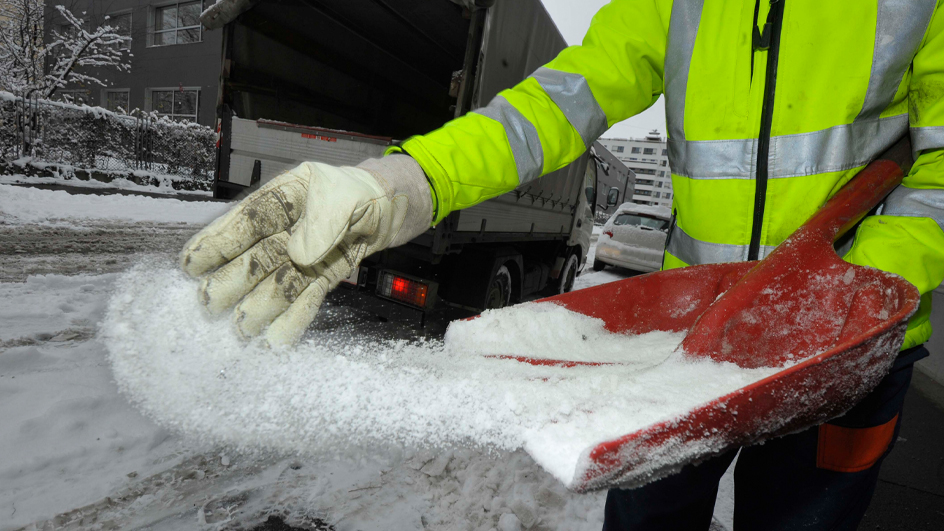 A worker spreads ice melt in a snowy environment