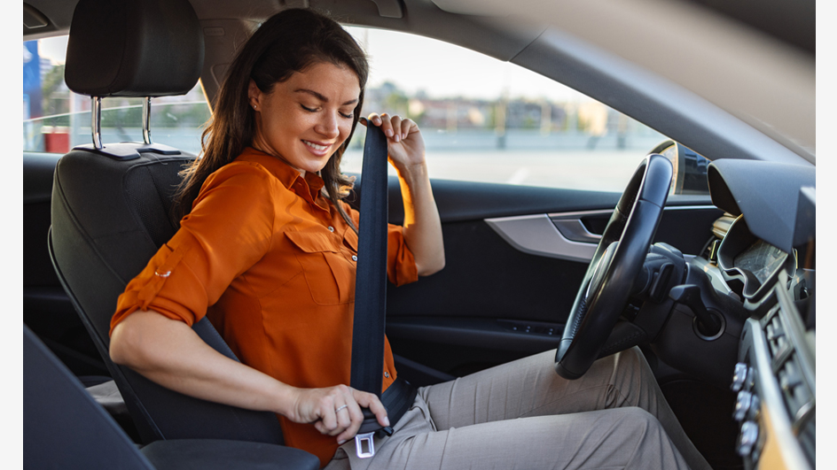 A woman puts on a seat belt after getting in the driver’s seat of a car.