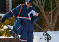A letter carrier in a blue winter uniform holds onto a handrail while walking down some steps.