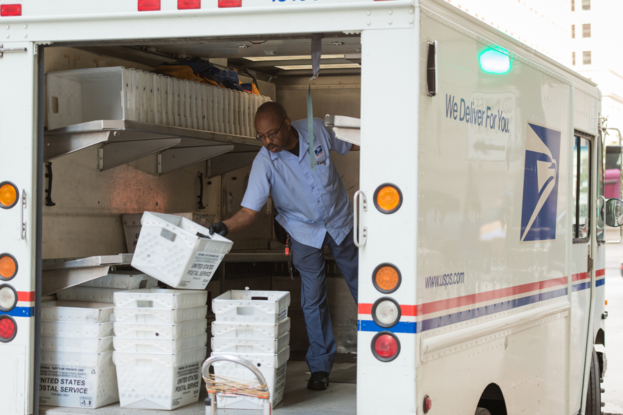 A male USPS employee standing in the back of a delivery truck stacking empty mail bins