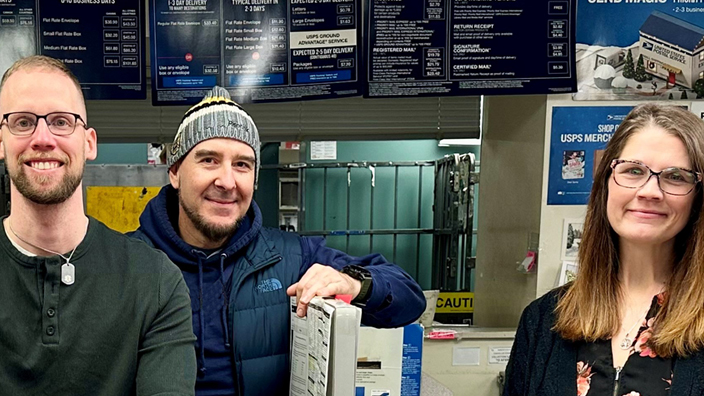 Four USPS employees standing behind a Post Office retail counter