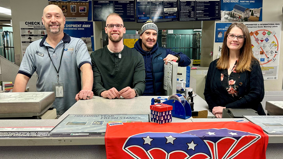 Four USPS employees standing behind a Post Office retail counter