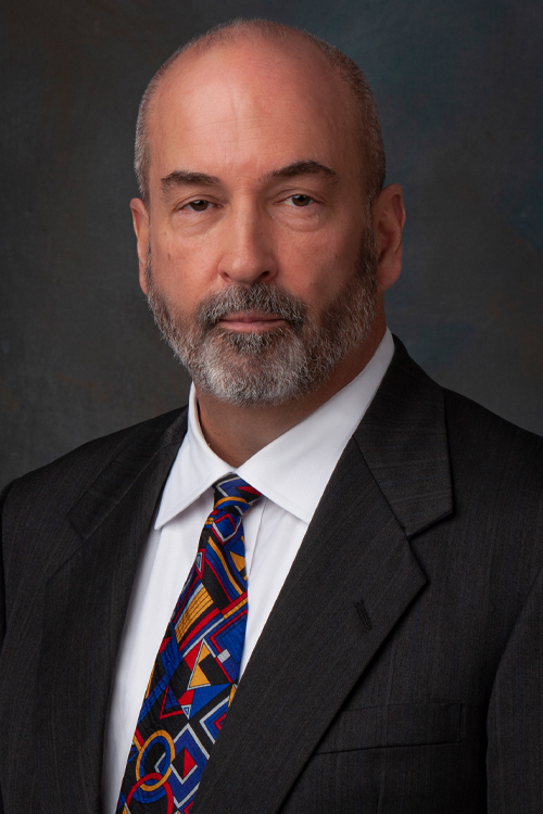 Portrait of a man with a beard wearing a dark suit jacket and a colorful tie