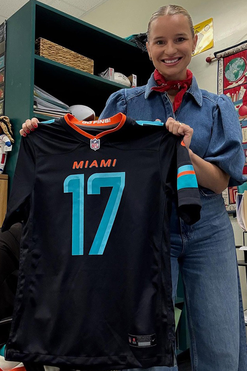 A woman holding up a black athletic jersey with the number 17 printed on the front in teal