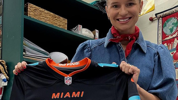 A woman holding up a black athletic jersey with the number 17 printed on the front in teal