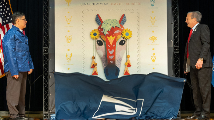 Two men stand on both sides of an enlarged image of the Year of the Horse stamp.