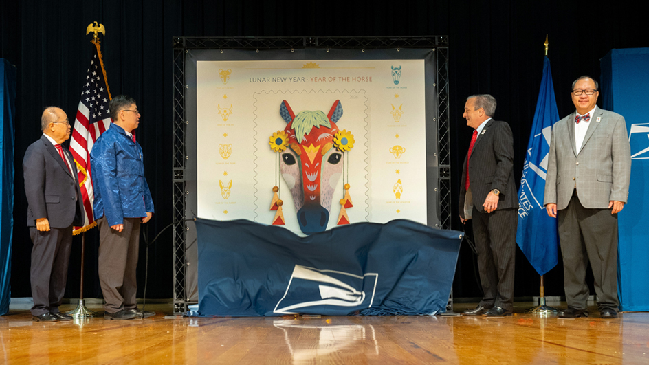 Two men stand on both sides of an enlarged image of the Year of the Horse stamp.