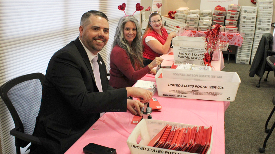 Three USPS employees sitting at a table stamping postmarks onto envelopes