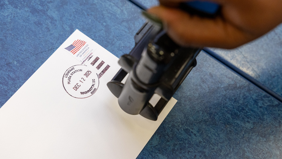 A hand applying a postmark to a white envelope