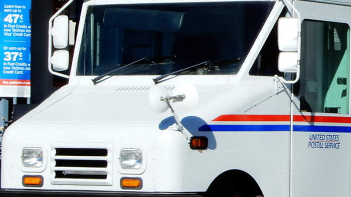A USPS delivery vehicle is parked near a gas station pump